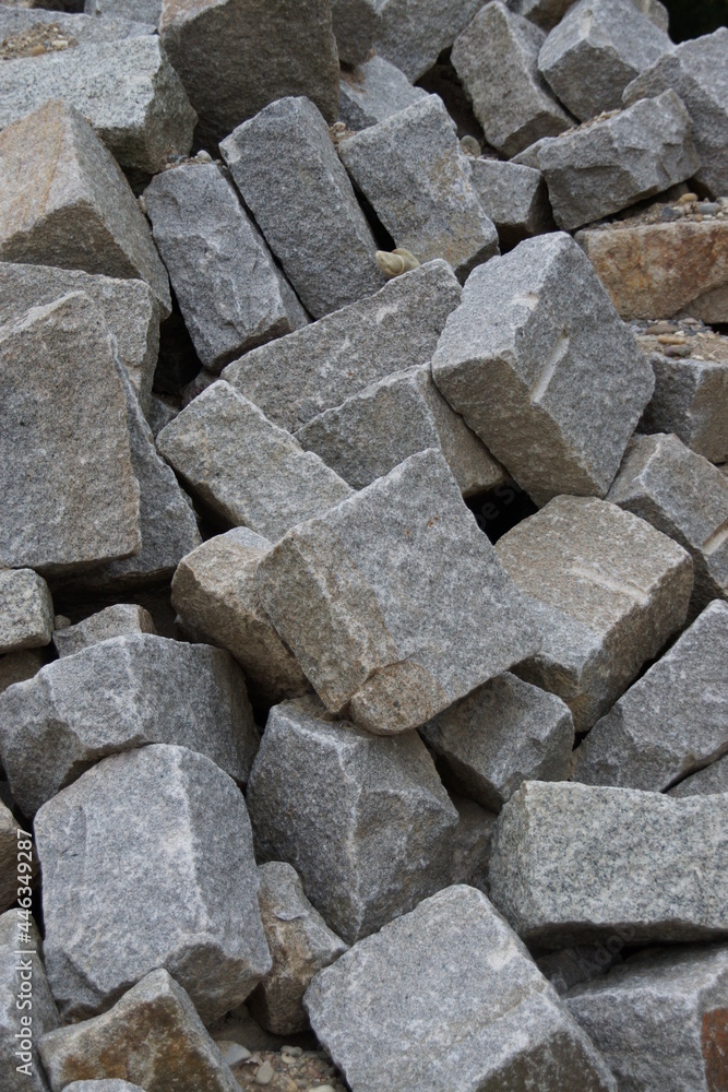 Aus harten Gestein hergestellte Bausteine mit identischen Abmessungen warten auf einer Baustelle darauf, dass sie eingebaut werden. Aus harten Gestein hergestellte Bausteine mit identischen Abmessungen warten auf einer Baustelle darauf, dass sie eingebaut werden.