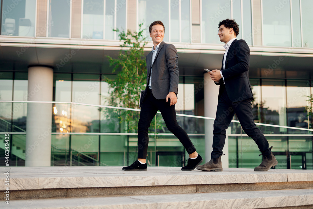 They discuss a new startup project and go to work. Satisfied colleagues work together. Businessmen young people work near the office in business suits. They discuss a new startup project and go to work. Satisfied colleagues work together. Businessmen young people work near the office in business suits.