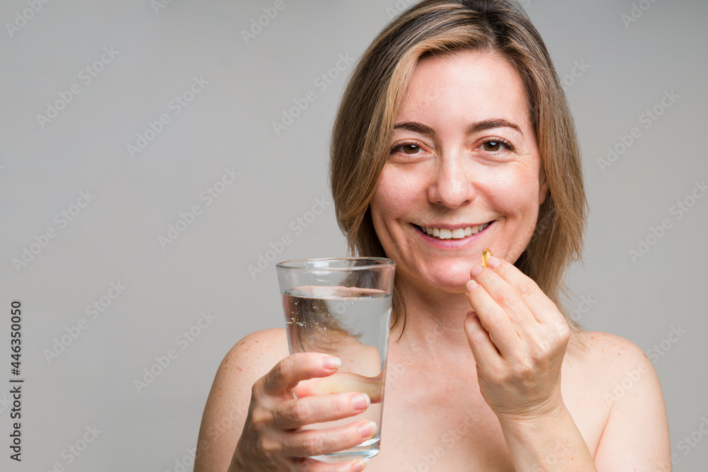 Happy mature woman taking a collagen pill Happy mature woman taking a collagen pill