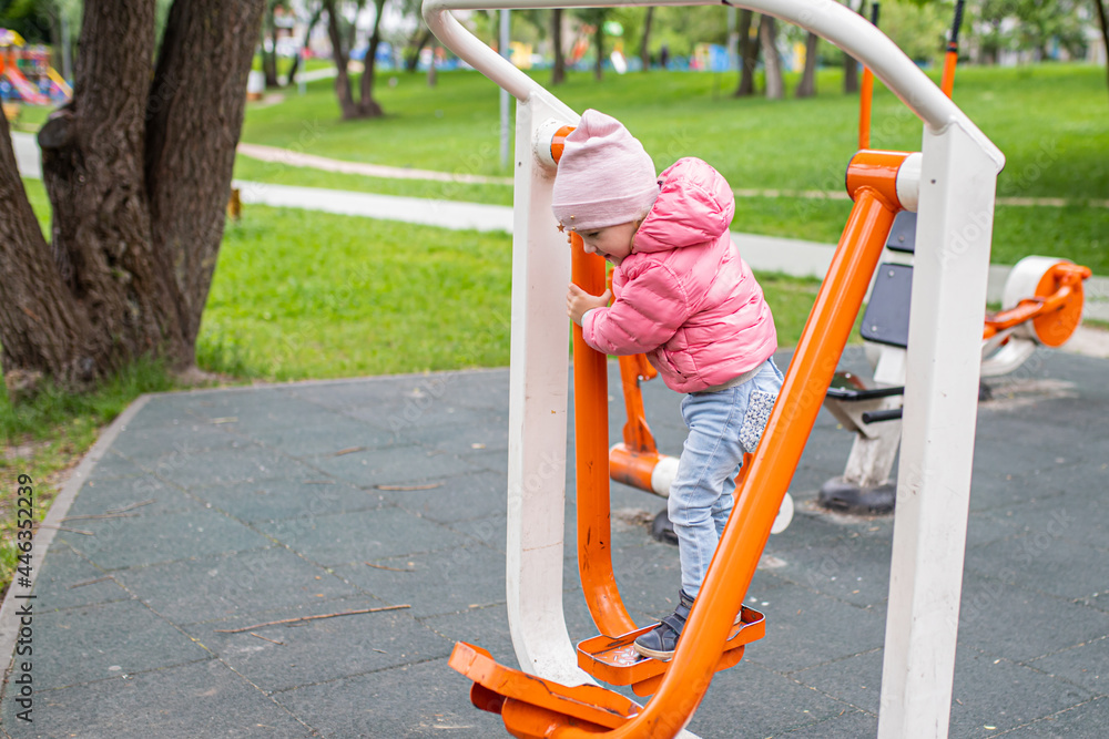 Fototapeta premium Girl doing exercises on the outdoor exercise machines FEET BREEDING resting their legs. Easy-to-use cardiovascular fitness equipment at sports ground in the city park