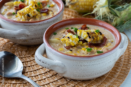 Close up view of a soup crock filled with chicken and corn chowder topped with grilled corn, ready for eating. photo