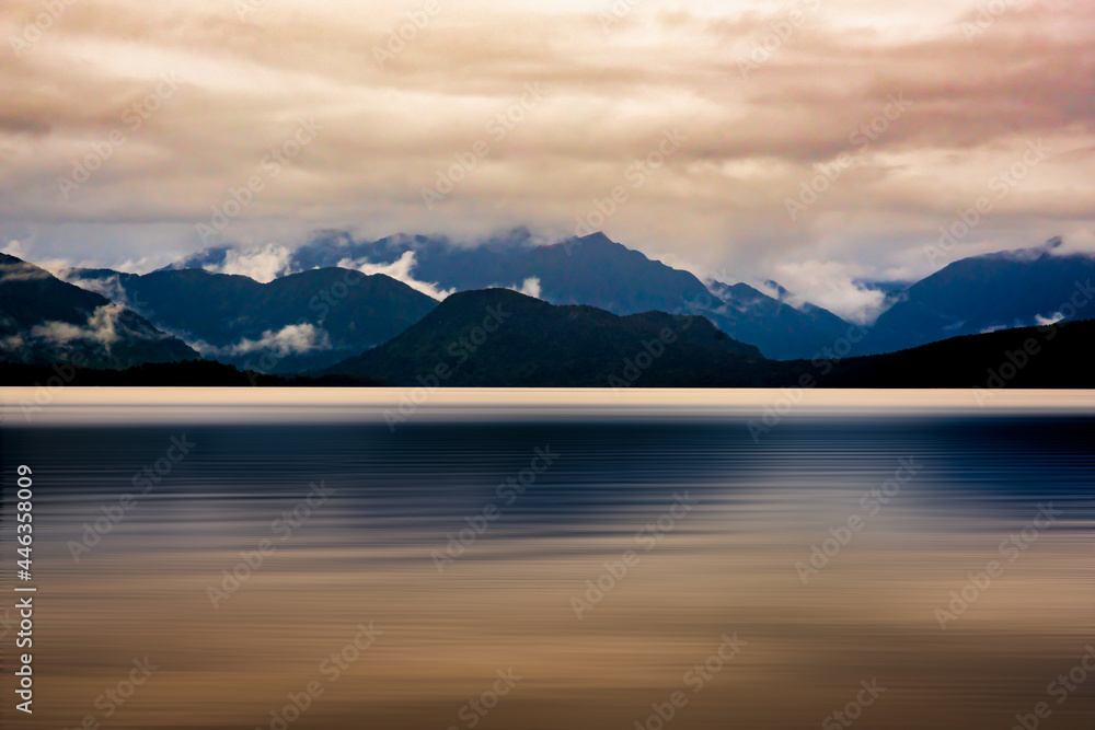 The mountain range bordering Lake Kaniere being reflected on the lake surface on  a dark and rainy wet cloudy moody late afternoon