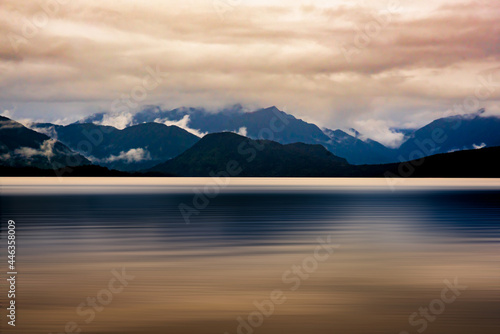 The mountain range bordering Lake Kaniere being reflected on the lake surface on a dark and rainy wet cloudy moody late afternoon