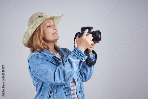 woman tourist in a hat uses a camera, takes a picture. Isolate on gray background © evafesenuk