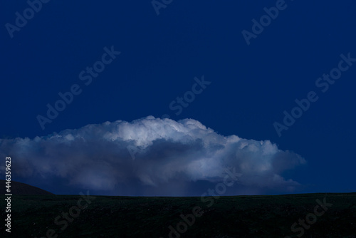 View of field with white fluffy clouds in blue sky at sunrise