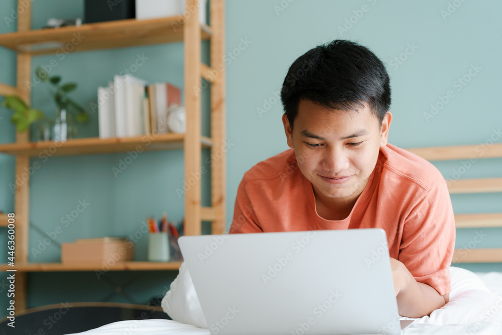 Asian man using a computer laptop while lying in a bedroom in the morning. Asian man using a computer laptop while lying in a bedroom in the morning.