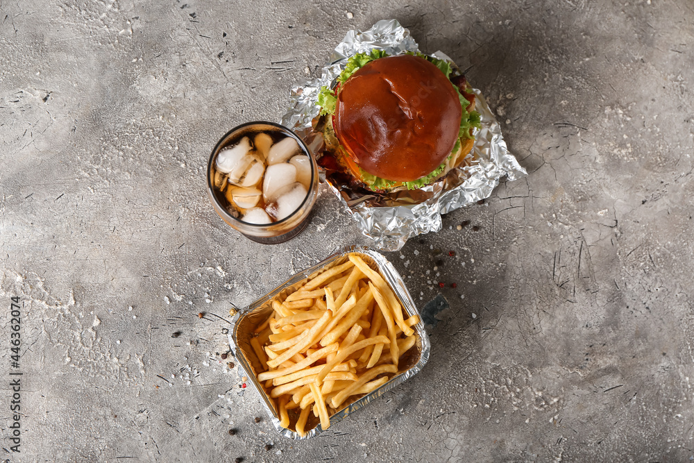 Box with tasty french fries, burger and glass of beverage on grunge background Box with tasty french fries, burger and glass of beverage on grunge background