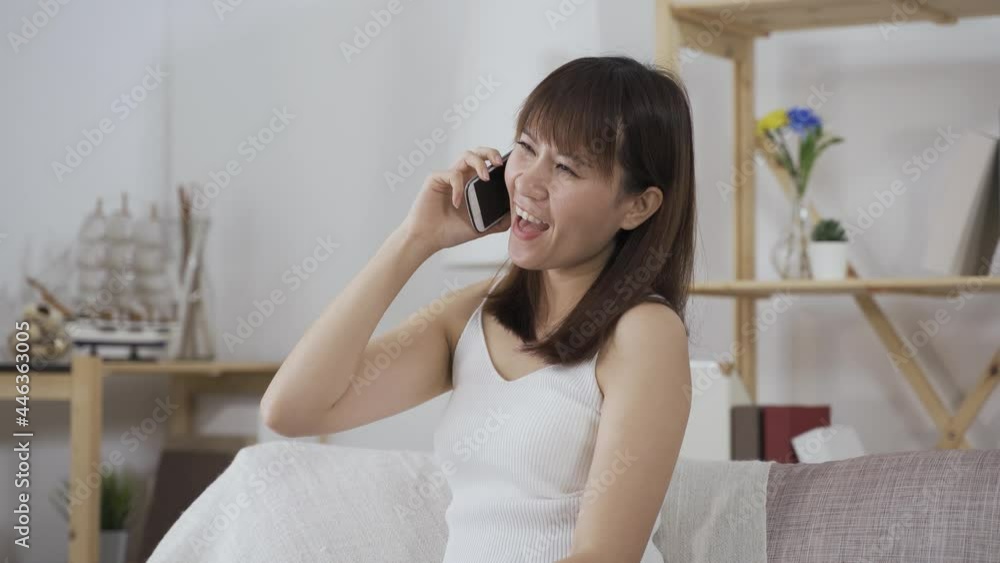 gorgeous taiwanese girl in white tank top taking to friend on phone happily with hand gestures at home. gorgeous taiwanese girl in white tank top taking to friend on phone happily with hand gestures at home.
