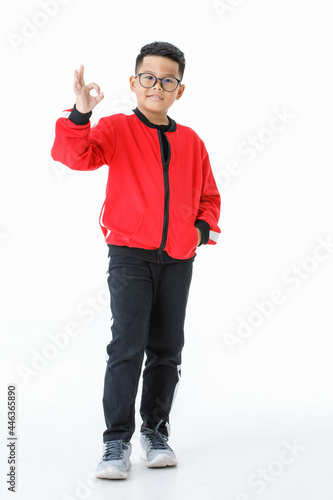 Funny cutout portrait of young healthy Asian boy on red jacket happily miling and raising right hand up to show OK sign as satisfying, confident, trust, ensure something and not worry