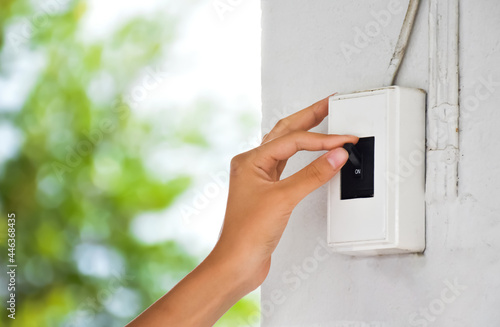 Homeowner is turning off the light switch on the wall of the house, concept for saving money and protect surrounding environment. Soft and selective focus.
