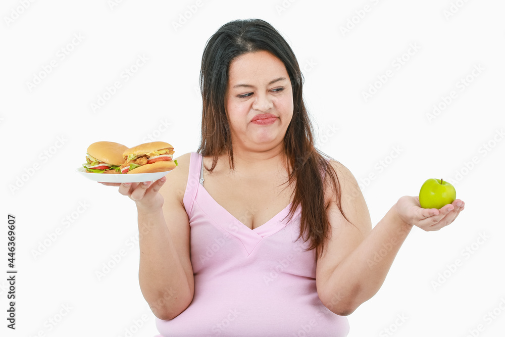 Isolated studio shot of Asian concentrate stress big fat overweight girl hate and does not like healthy organic green apple in hand and may choose temptation unhealthy hamburgers on white background Isolated studio shot of Asian concentrate stress big fat overweight girl hate and does not like healthy organic green apple in hand and may choose temptation unhealthy hamburgers on white background