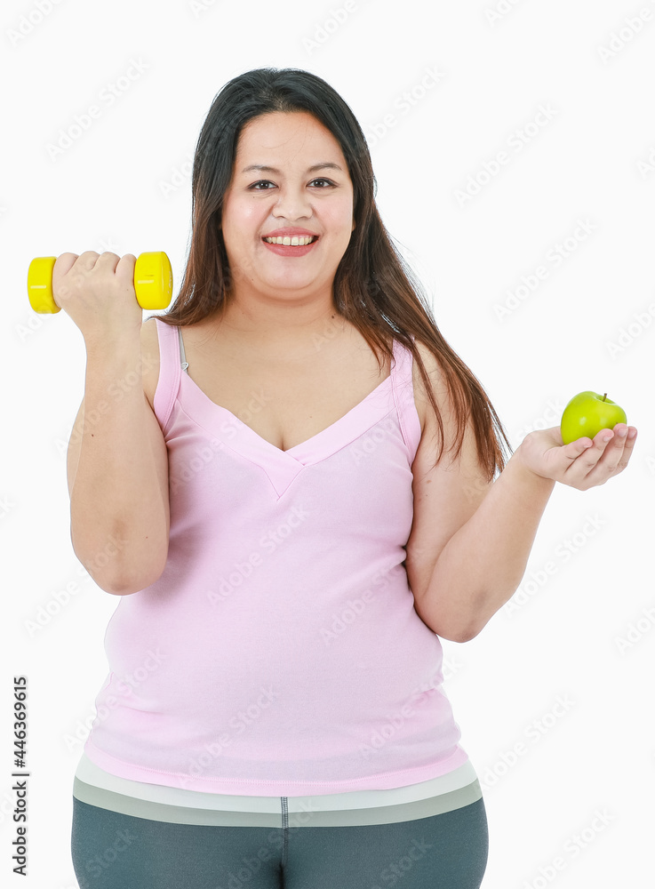 Portrait isolated studio shot of Asian happy healthy big fat oversize girl in sport clothing standing smiling lifting yellow dumbbell and hold organic green apple in other hand on white background Portrait isolated studio shot of Asian happy healthy big fat oversize girl in sport clothing standing smiling lifting yellow dumbbell and hold organic green apple in other hand on white background