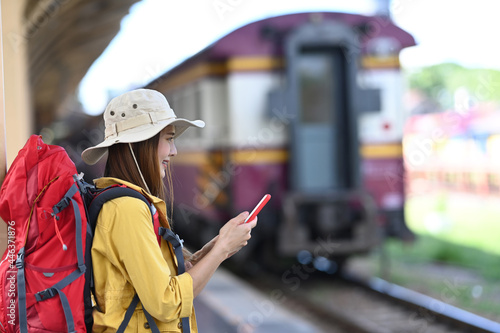 Young woman traveler with backpack using smart phone and standing in the railway. © Prathankarnpap