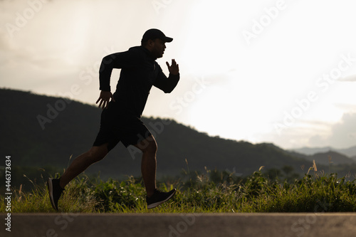 Silhouette Young man wearing sportswear running outdoor nature mountain background. Man jogging on the country side road. Training athlete outdoor concept.