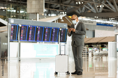 Young businessman wearing mask to protect flu coronavirus Covid-19.He drag luggage walking in terminal. Tourist in airport terminal using smartphone check in at counter. photo