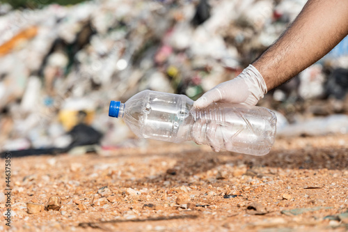 Photos Hand holding a plastic bottle in front of a large mountain and a pile of trash