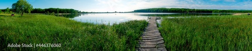 Panorama of a wooden path for fishermen. Green thickets on the shore of the pond.