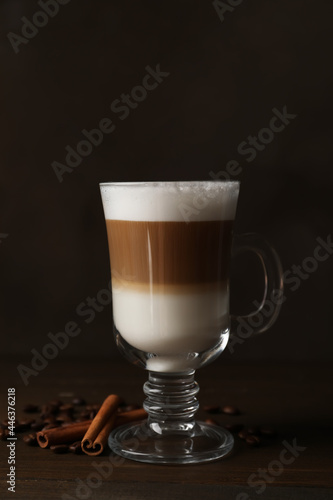 Hot coffee with milk in glass cup, beans and cinnamon sticks on wooden table