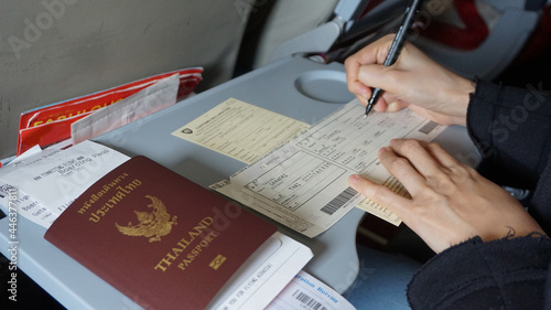 Hand filling trip immigration form on plane with passport give information foriegn entry card photo