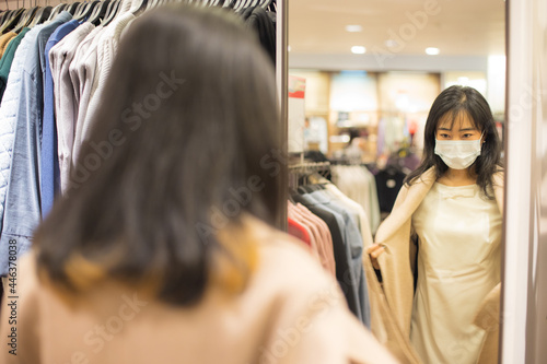 Asian woman standing in front of mirror in shop while shopping.