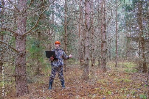 Forest engineer works in the forest with a computer. An ecologist in a young forest holds a computer in his hands.