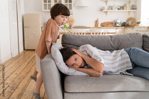 Quadro em tela Stressed exhausted mother lie on sofa in kitchen desperate about stubborn kid son, upset annoyed mom tired of naughty child misbehave and noise