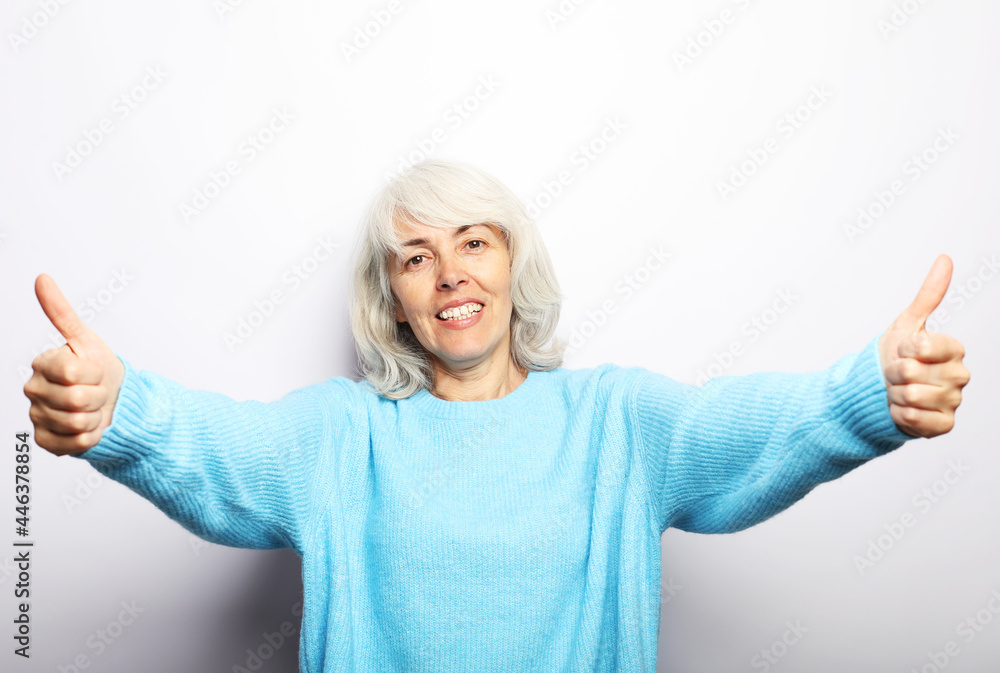 Good mood happy smiling positive elderly woman with white hair, wearing blue sweater show thumbs up. Good mood happy smiling positive elderly woman with white hair, wearing blue sweater show thumbs up.