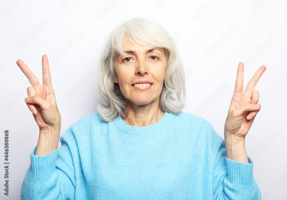 Good mood happy smiling positive elderly woman with white hair, wearing blue sweater show v-sign. Good mood happy smiling positive elderly woman with white hair, wearing blue sweater show v-sign.