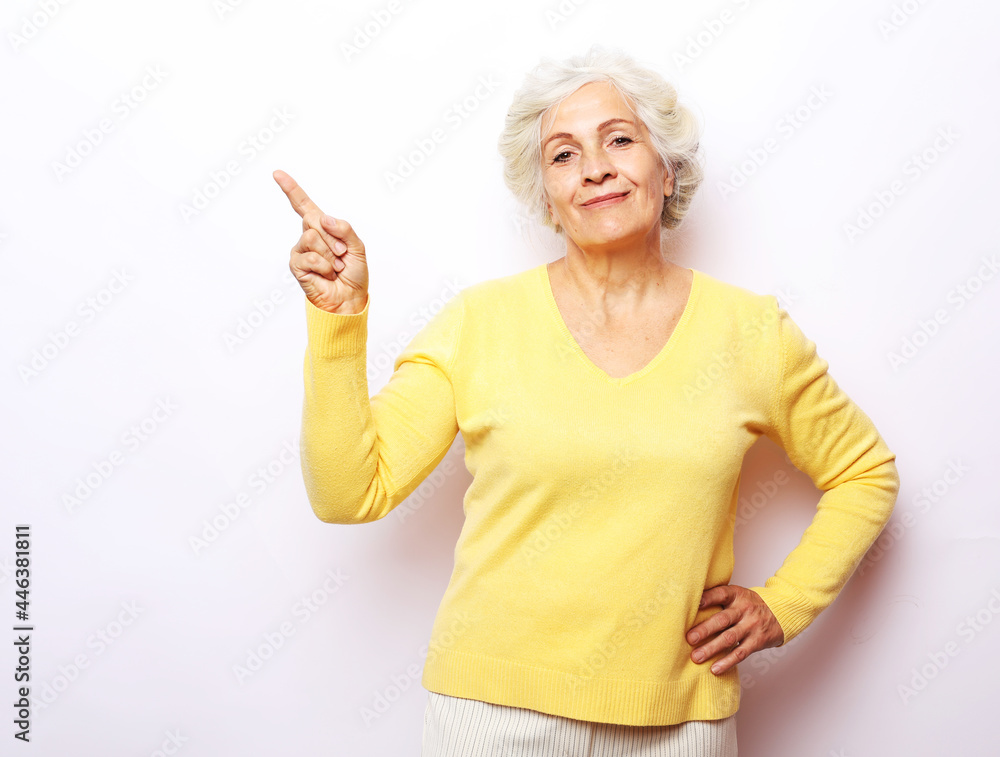 Smiling senior gray-haired woman isolated on gray studio background pointing with finger at blank copy space aside Smiling senior gray-haired woman isolated on gray studio background pointing with finger at blank copy space aside