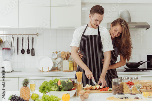Happy couple love cooking together in kitchen. Young loving man and woman laughing while cooking healthy food at home.