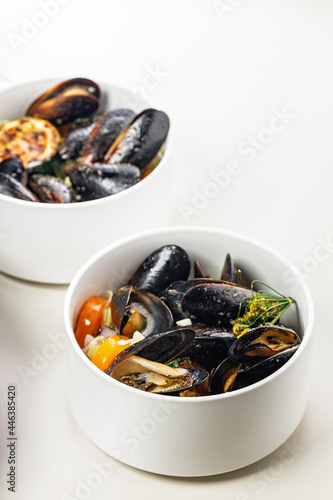 Mussels with vegetables and herbs in a white bowl on a light background. Healthy, delicious and tasty organic seafood. Traditional Mediterranean cuisine. Vertical food photography