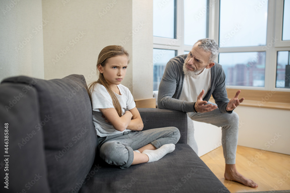 Gray-haired bearded man talking to his kid while she looking moody Gray-haired bearded man talking to his kid while she looking moody