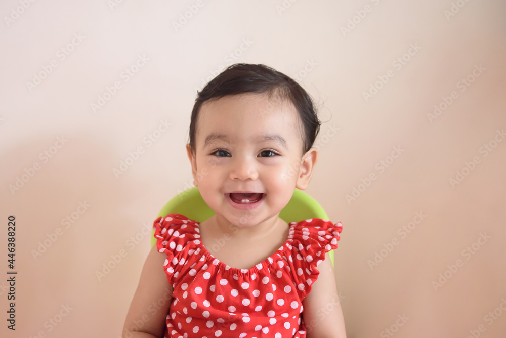 Portrait of a smiling cute little Asian baby girl wear red dress siting on bed and looking at camera, isolated on background, baby expression concept Portrait of a smiling cute little Asian baby girl wear red dress siting on bed and looking at camera, isolated on background, baby expression concept