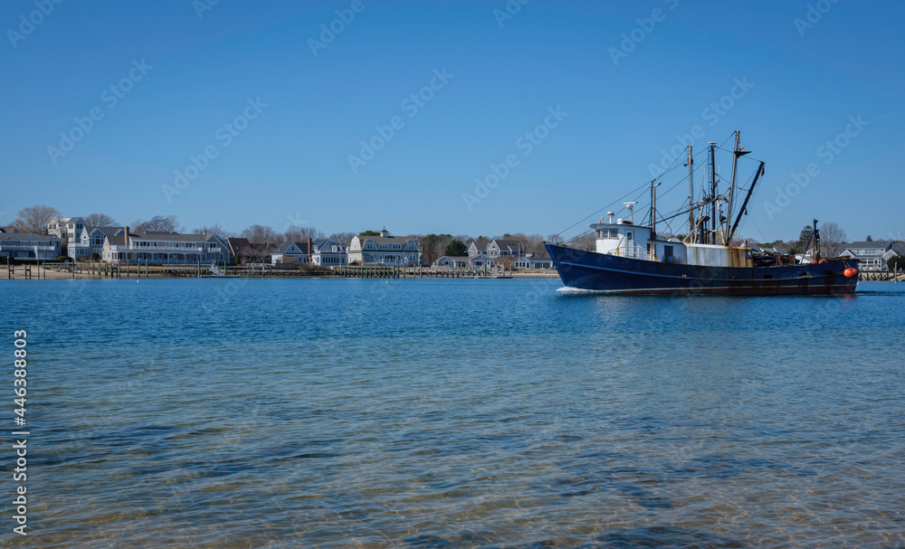 Commercial fishing boat sailing on blue sea water canal to the left. Peaceful seascape of the maritime village with ship passing on a bright summer day.