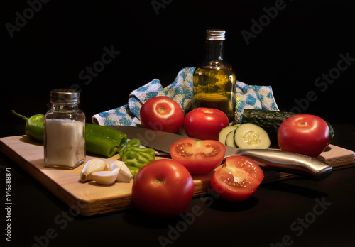 Traditional summer cold tomato soup gazpacho ingredients on a wood plank -Tomatoes, pepper, cucumber, garlic, salt and olive oil - black background - mediterranean, spanish food concept