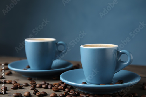 Cups of tasty espresso and scattered coffee beans on wooden table