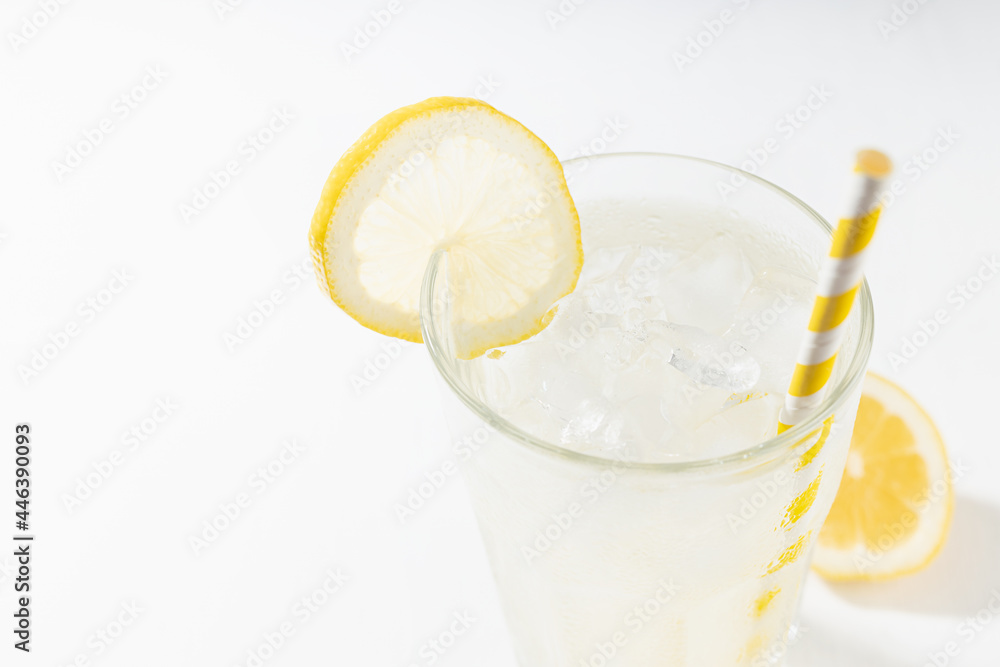 Fresh summer classic lemonade in glass with straw, ice, lemon slice on soft light white wood table in sunlight, crop, closeup. Fresh summer classic lemonade in glass with straw, ice, lemon slice on soft light white wood table in sunlight, crop, closeup.