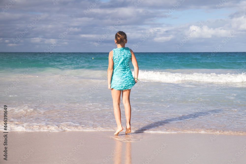 Little girl in a blue dress stands on a beach.