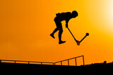 Unrecognizable teenage boy silhouette showing high jump tricks on scooter against orange sunsetwarm sky at skatepark. Sport, extreme, freestyle, outdoor activity concept