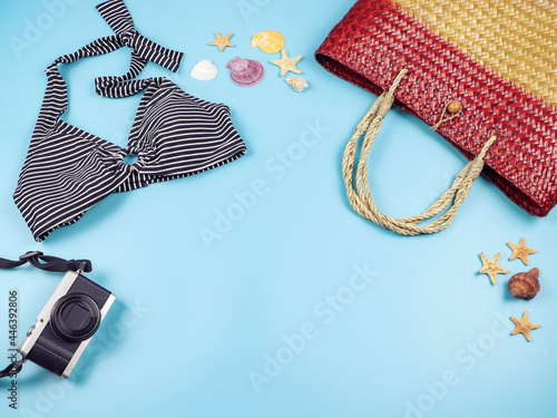 flat lay of woven or rattan bag, bikini and camera on blue background, decorated with sea shells and starfishes, copy space. Summer beach vacation background.