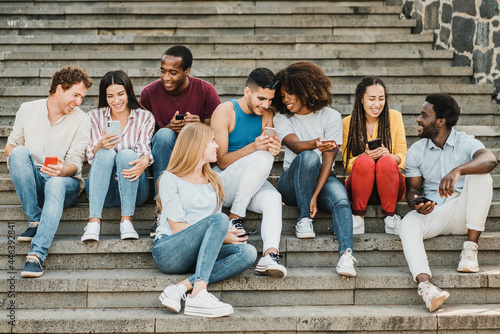 Multiethnic friends sitting on steps and using smartphones