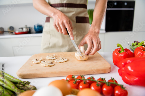 Cropped view of guy preparing fresh natural bio weight loss meal cutting mushroom at light white kitchen home indoors