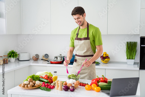 Photo portrait young man in apron cooking vegetables salad with laptop