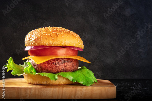 Burger, side view with copy space. Hamburger with a fat beef patty, green salad, cheese, tomato and onion, shot on a dark background