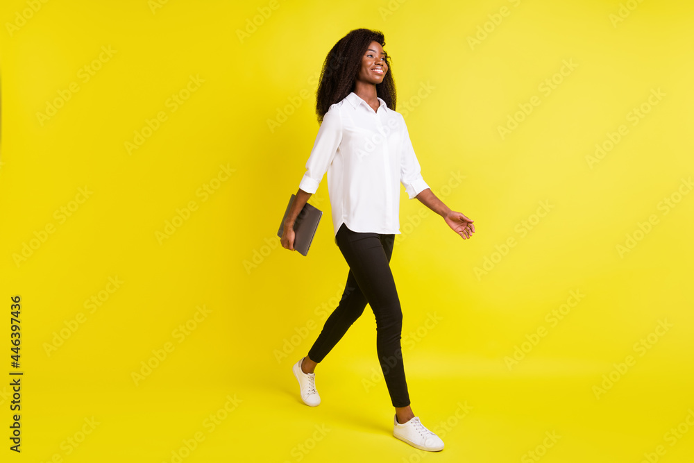 Full length body size photo smiling girl walking forward keeping laptop looking blank space isolated bright yellow color background Full length body size photo smiling girl walking forward keeping laptop looking blank space isolated bright yellow color background