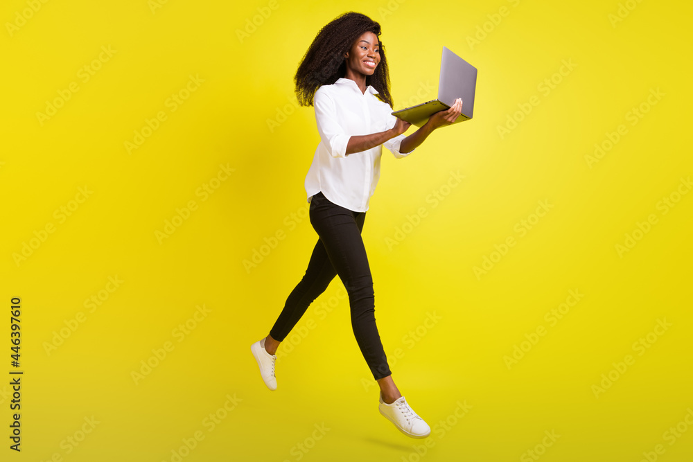 Full length photo of happy dark skin woman jump up walk hold laptop isolated on yellow color background Full length photo of happy dark skin woman jump up walk hold laptop isolated on yellow color background