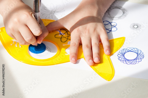 child drawing spirograph pattern with spirograph kit, flat lay.