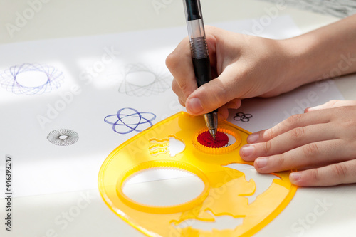 child drawing spirograph pattern with spirograph kit, flat lay.