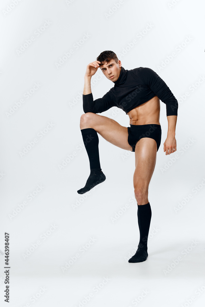 a young guy in shorts, a sweater and socks raised his leg up on a light background in full growth