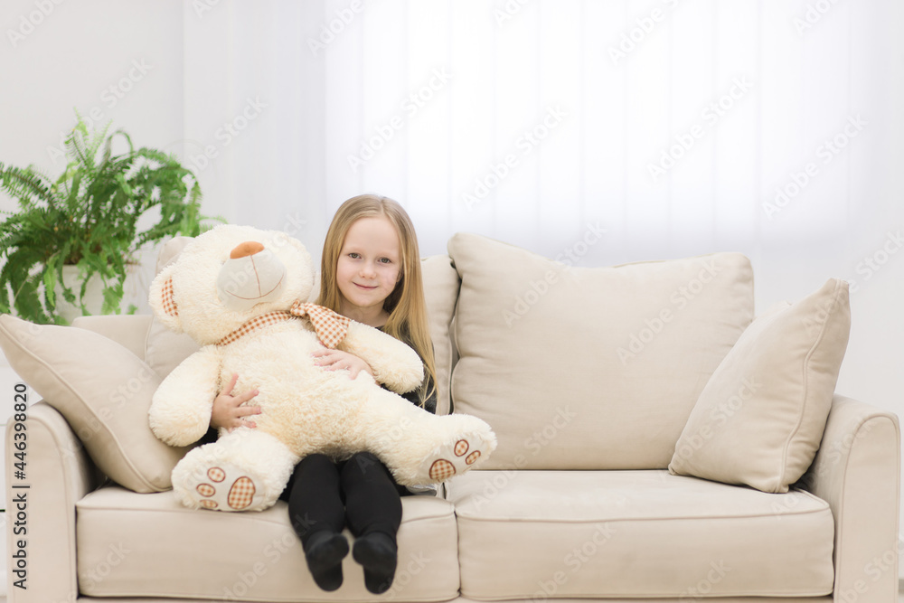 Small smiling girl sitting on the sofa with her toy teddy bear photo.